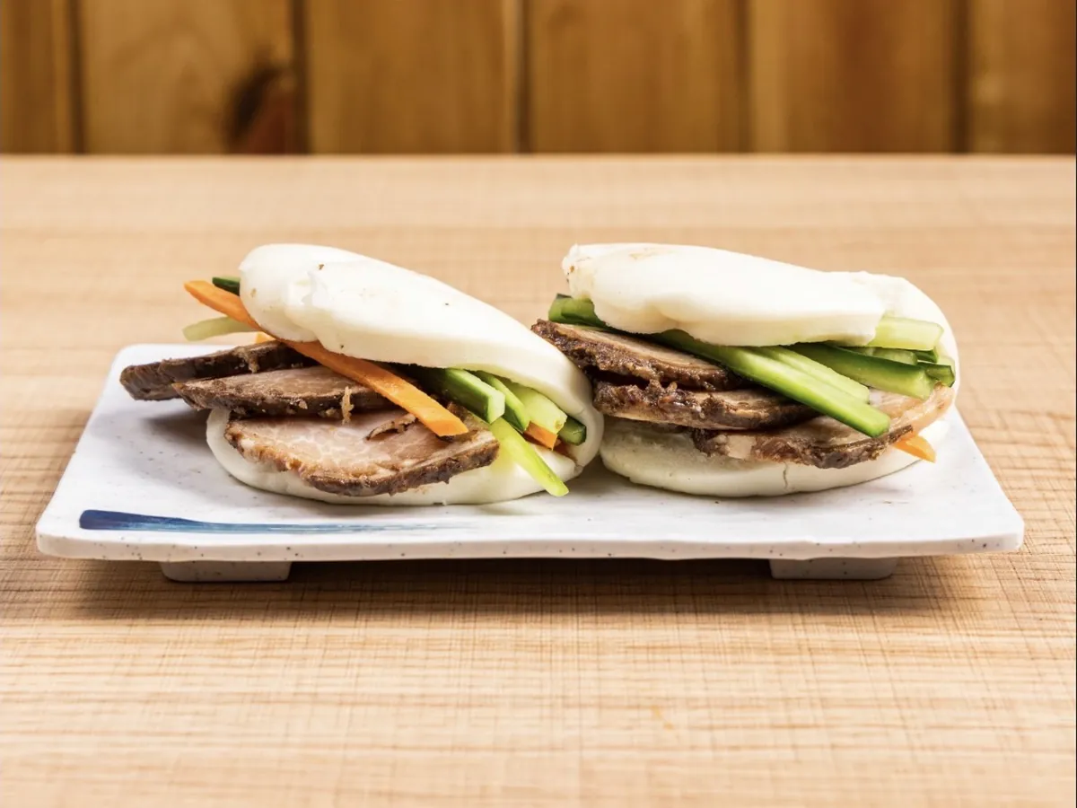 Two chashu pork buns filled with sliced braised pork, cucumber and carrot on a white plate