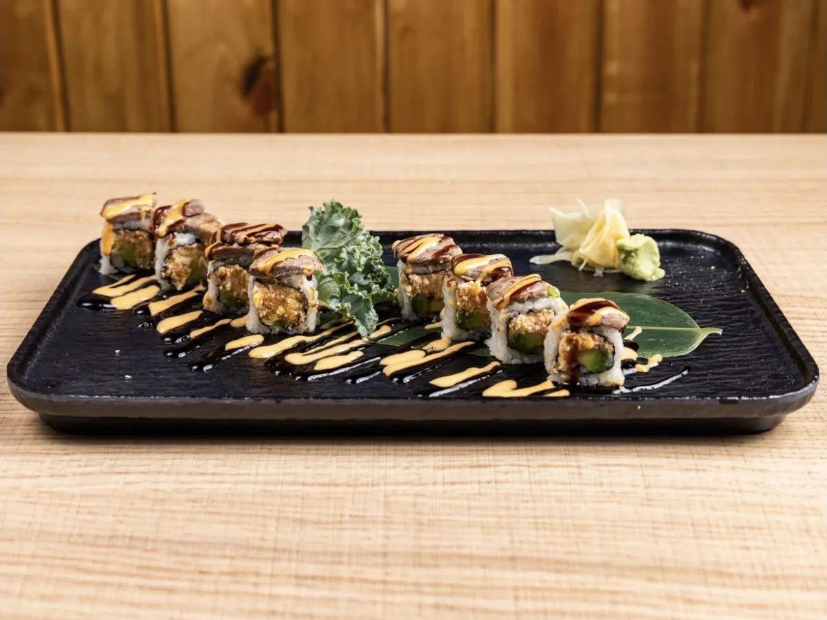 Cowboy Roll topped with slices of seared hibachi steak and crispy onion under spicy mayo and eel sauce