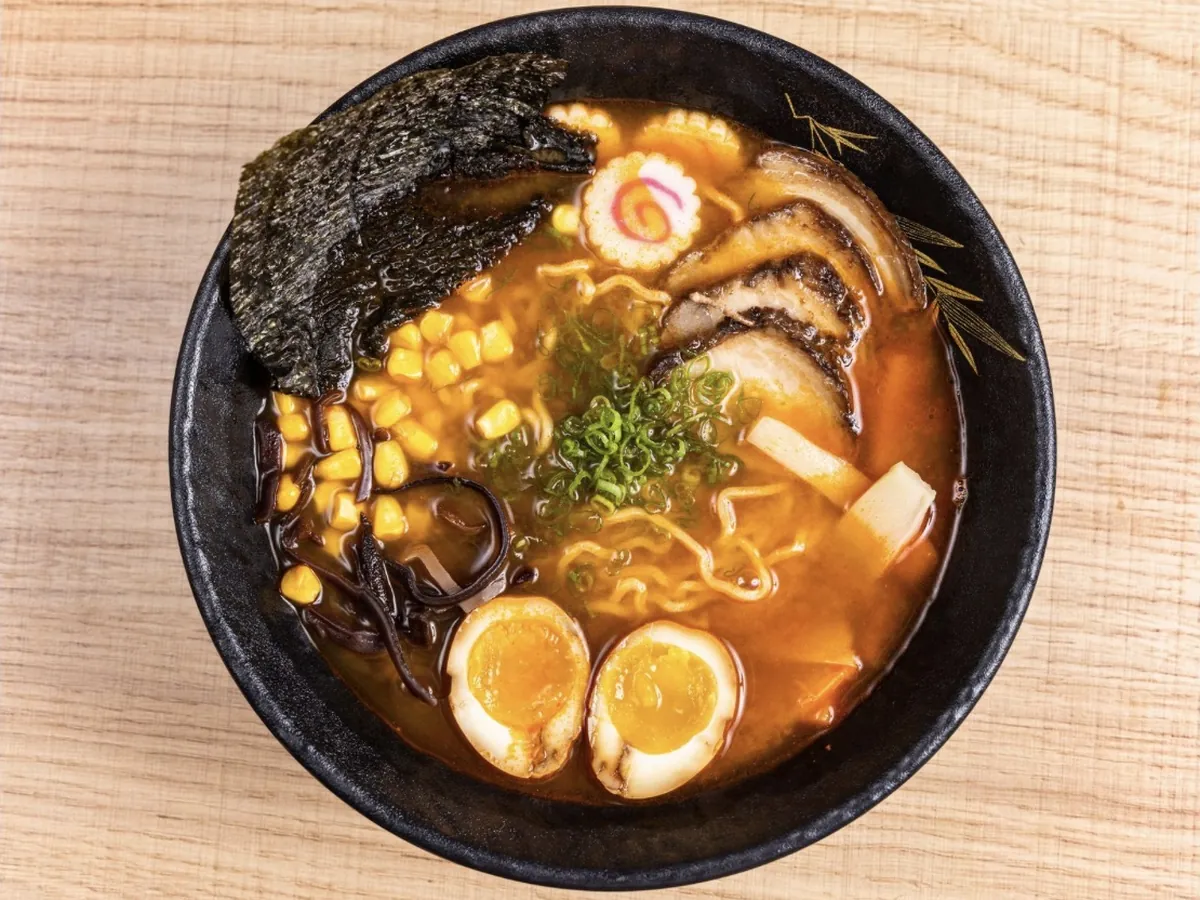 Bowl of spicy tonkotsu ramen with chashu pork, soft egg halves, corn, bamboo shoot, narutomaki and nori