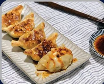 Pan-fried gyoza dumplings on a ceramic plate with a small dish of dipping sauce