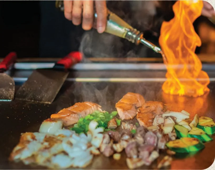 Hibachi chef searing salmon and vegetables over open flame on the flat-top grill